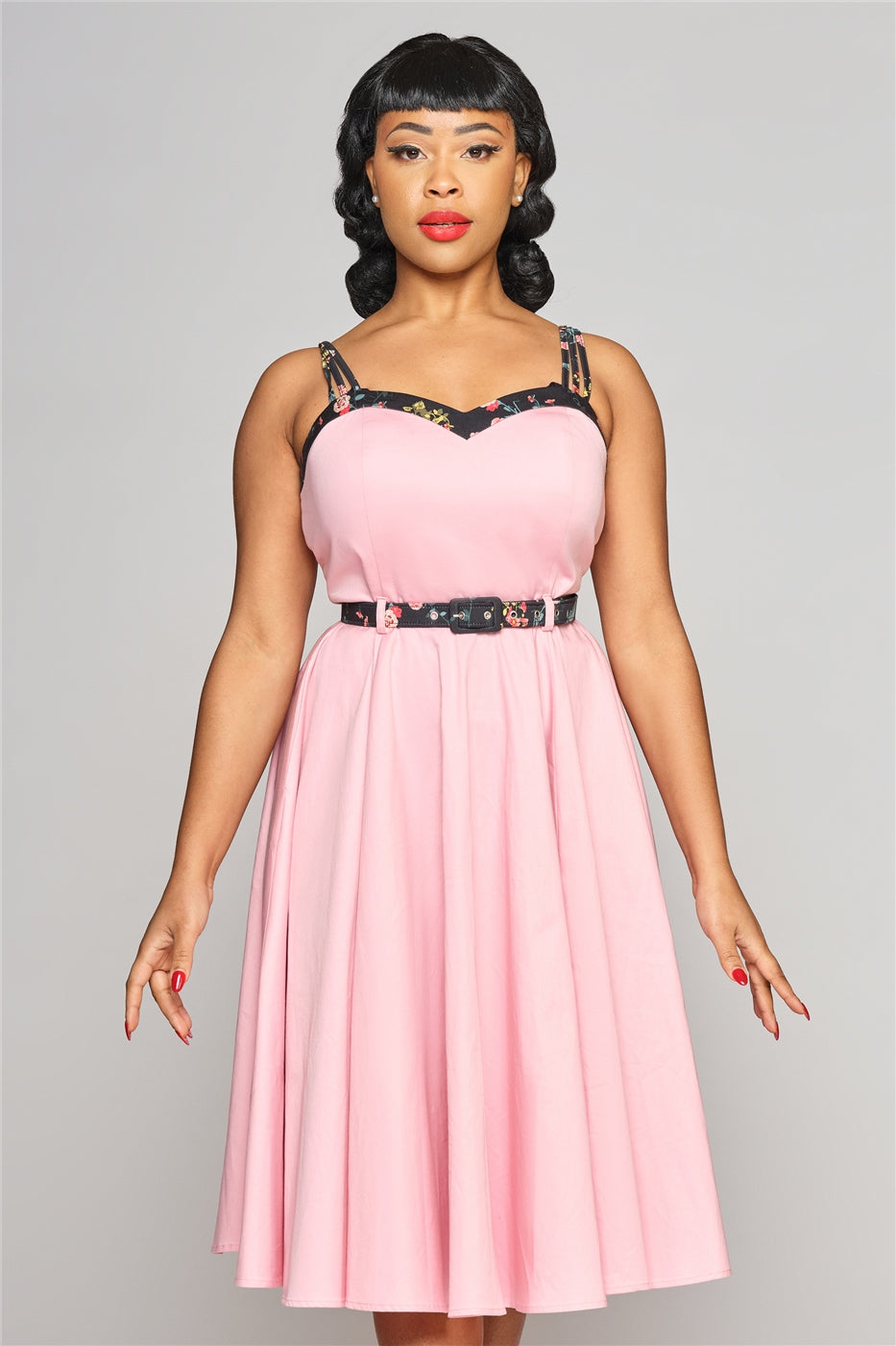 elegant woman standing wearing a pink 50s style dress with a sweetheart neckline and belt.