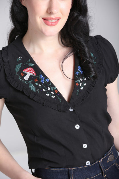 Close up of model wearing a black blouse with floral embroidered detail on the collar
