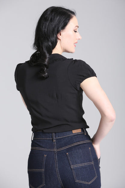 Back view of model wearing a semi fitted black viscose blouse with short sleeves