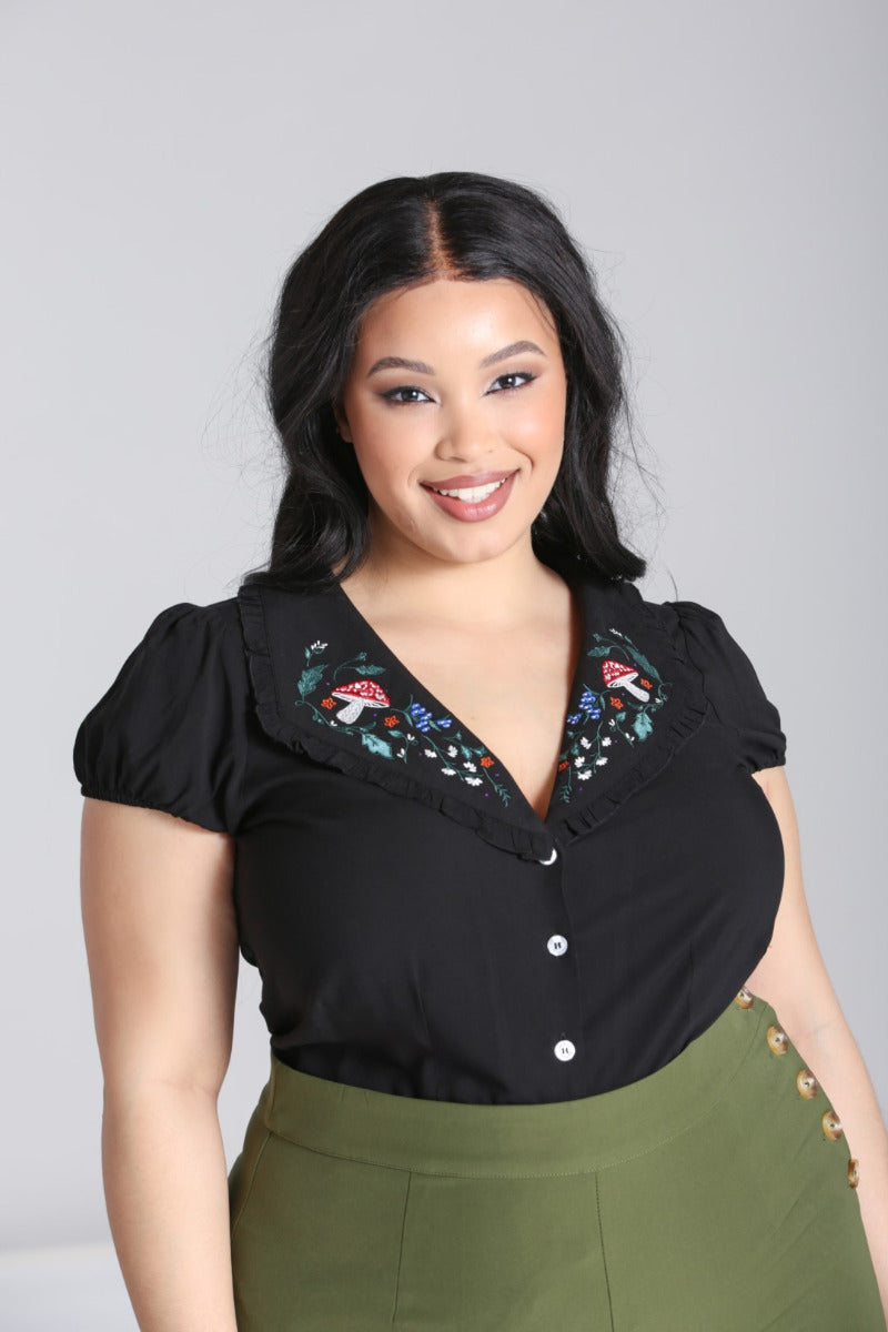 Happy smiling woman with dark hair and natural makeup wearing high waisted trousers and an embroidered blouse