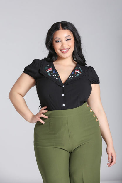 Beautiful plus size model wearing green high waisted swing trousers and a black blouse with an embroidered collar  standing with one hand on her hip.