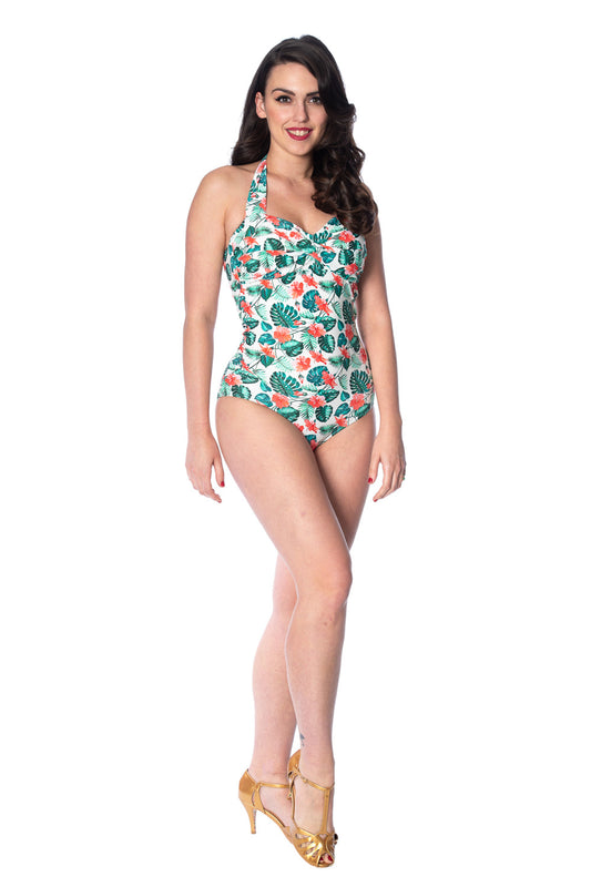 Dark haired woman standing wearing a tropical leaf and hibiscus pattern halter neck swimsuit