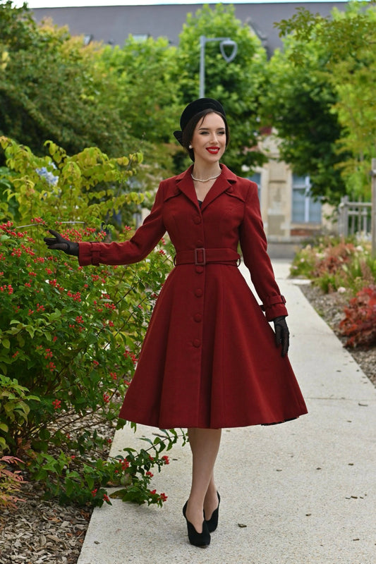 Woman in a deep terracotta coloured vintage coat standing in a garden.