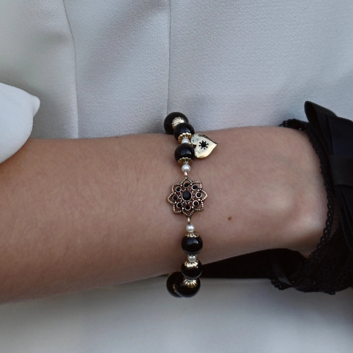 Close-up of a wrist wearing a beaded bracelet with decorative elements on a neutral background