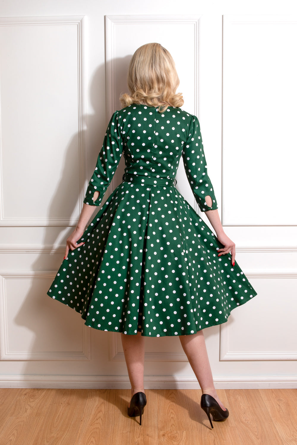 Woman wearing a green dress with white polka dots against a white wall.