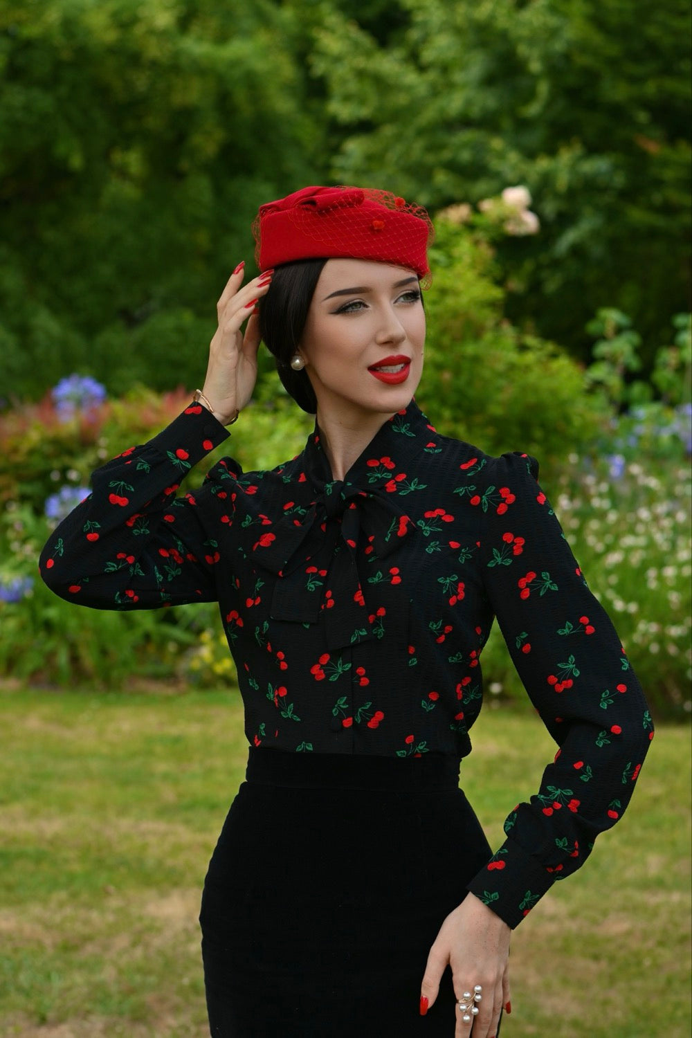 Woman wearing a black blouse with red cherry pattern and a red beret outdoors.