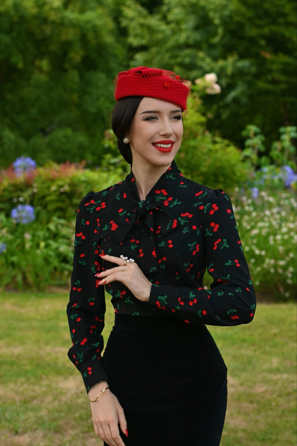 Woman wearing a red hat and black patterned dress in a garden setting