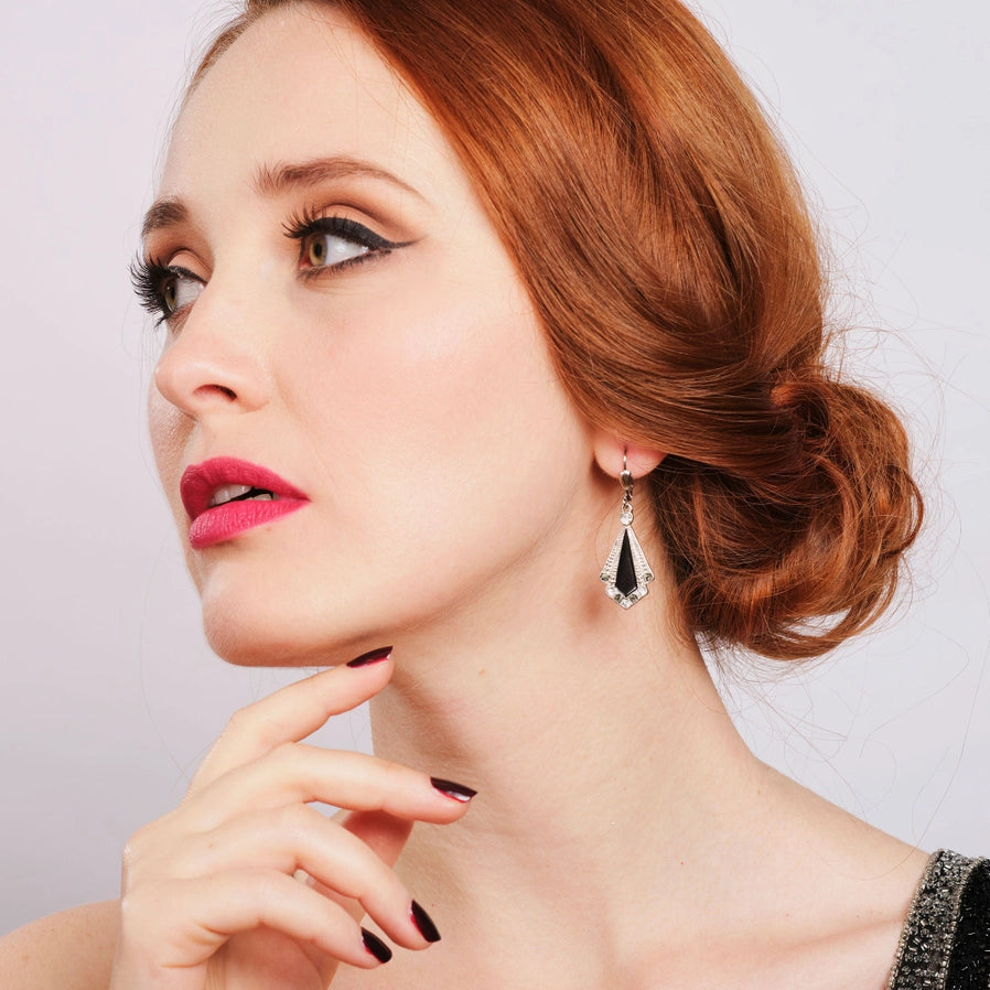 Model wearing a 1920s-inspired Art Deco earring by Lovett & Co, featuring a fan-shaped black enamel and silver-tone design with crystal accents, styled with vintage-inspired makeup and hair.