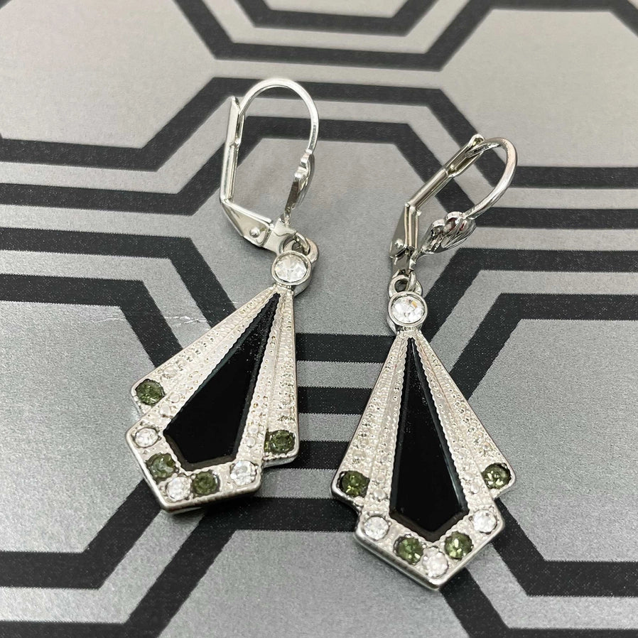 1920s-inspired Art Deco earrings by Lovett & Co, featuring a fan-shaped design with black enamel and silver-tone metal, accented with crystals and green stones, displayed on a geometric background.