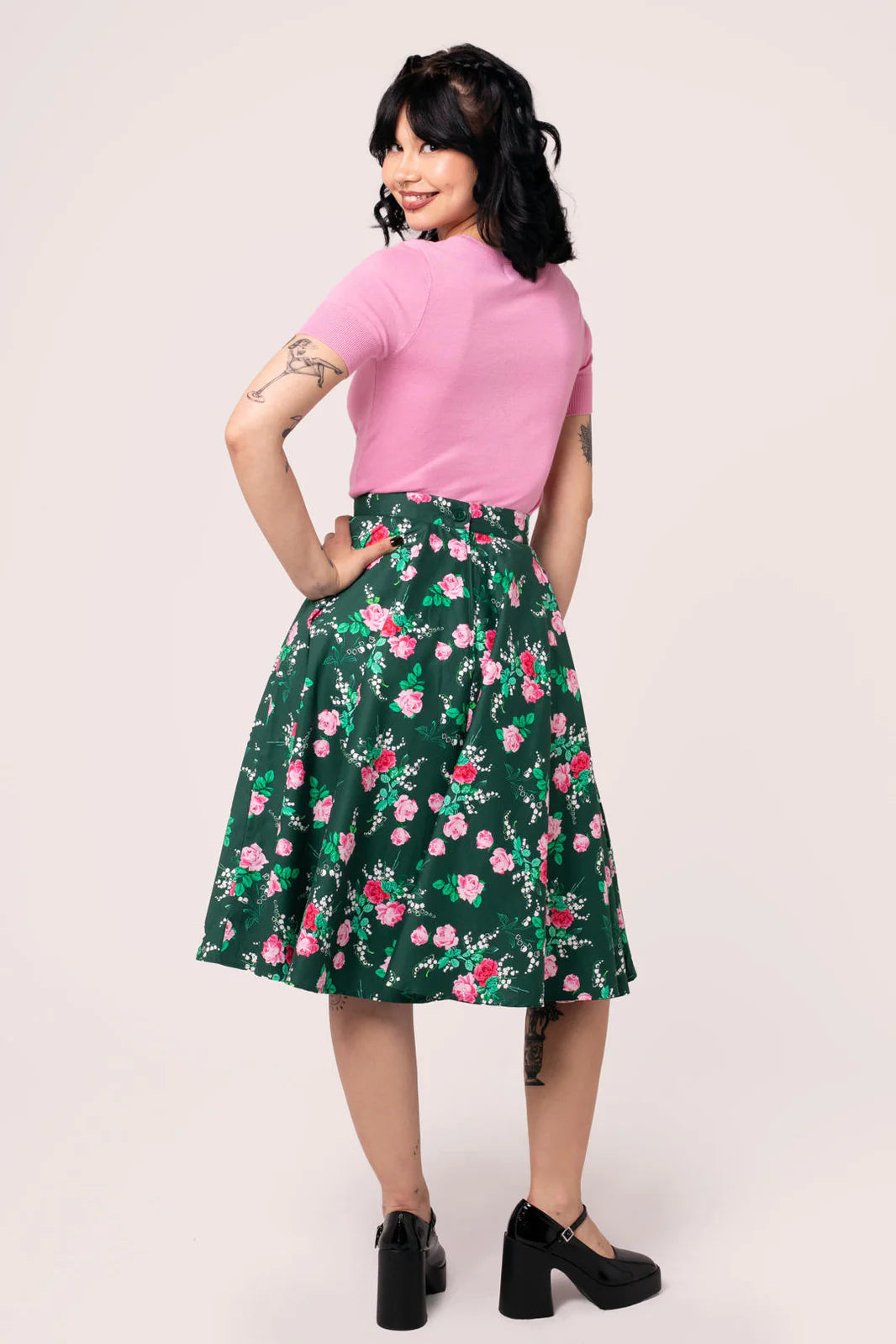 Woman wearing a pink top and green floral skirt on a white background