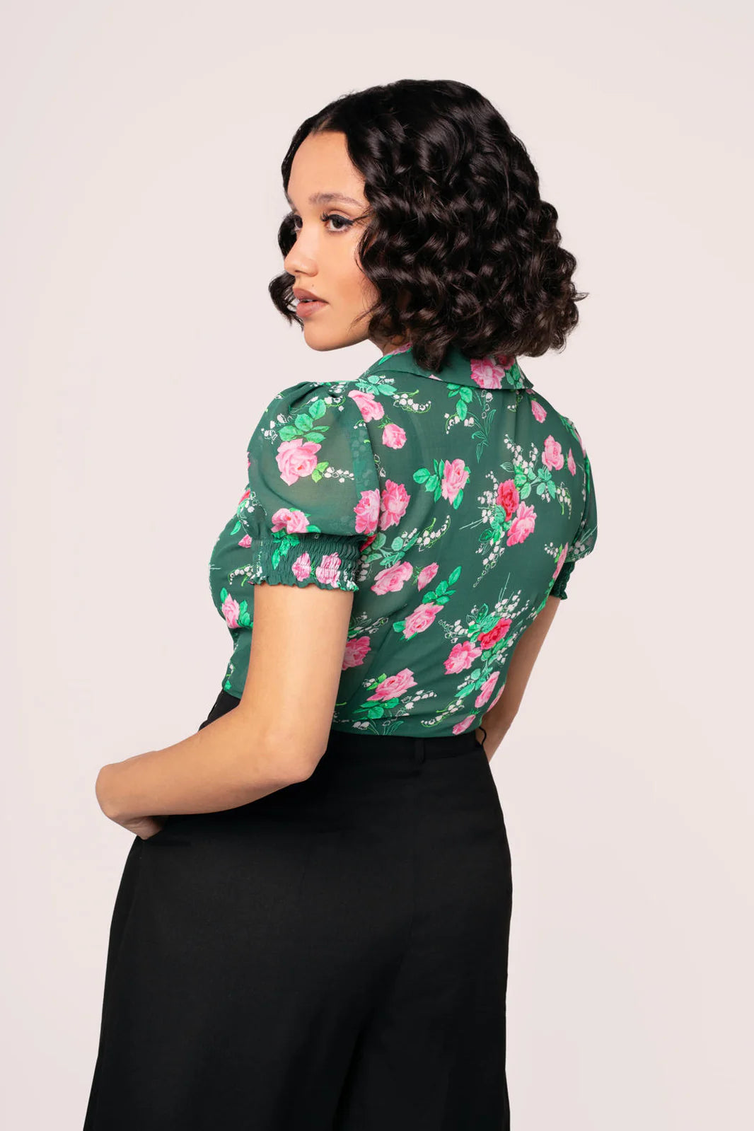 Woman wearing a green floral blouse with black pants on a plain background