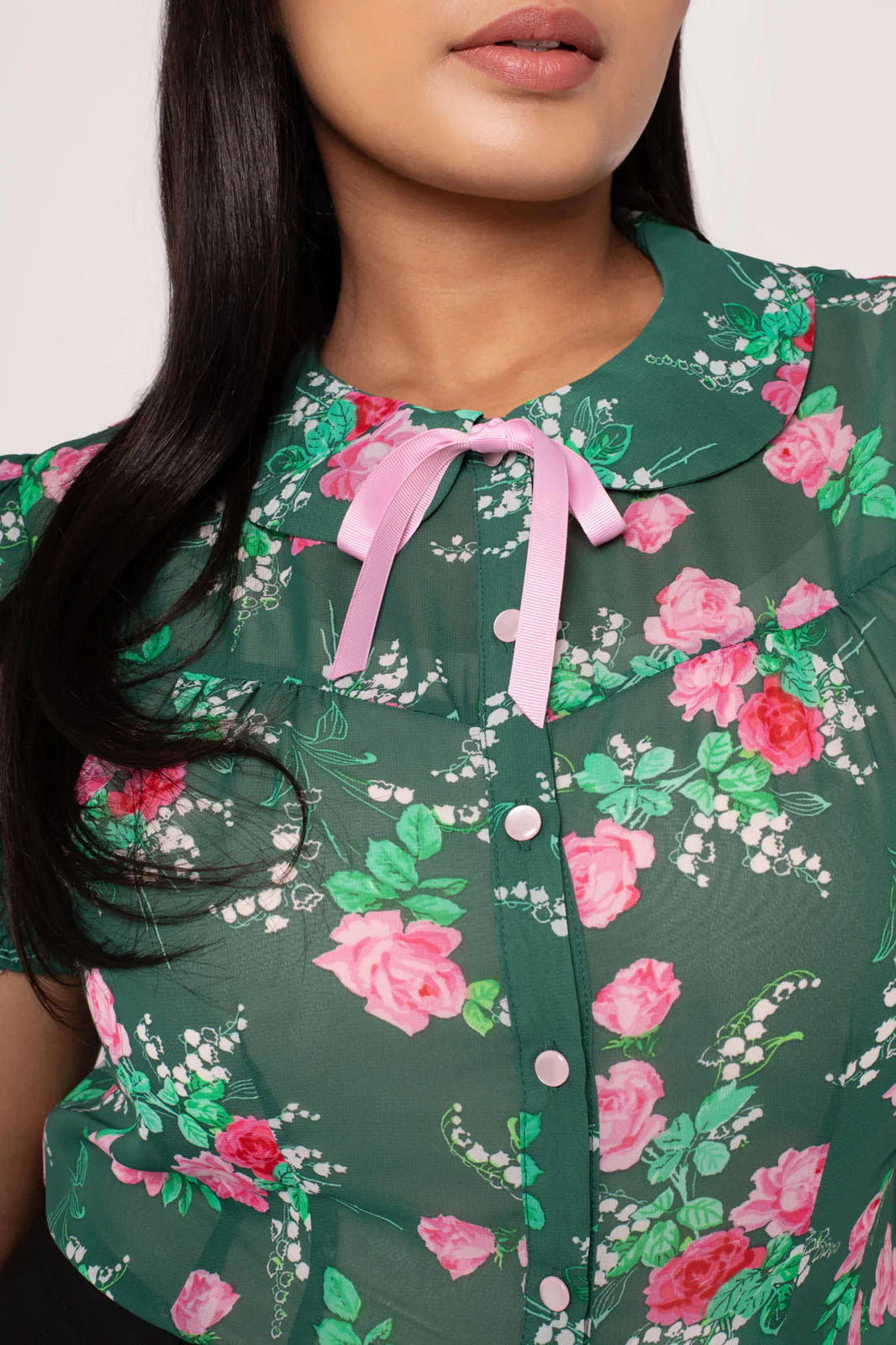 Woman wearing a green floral blouse with pink roses and green leaves.