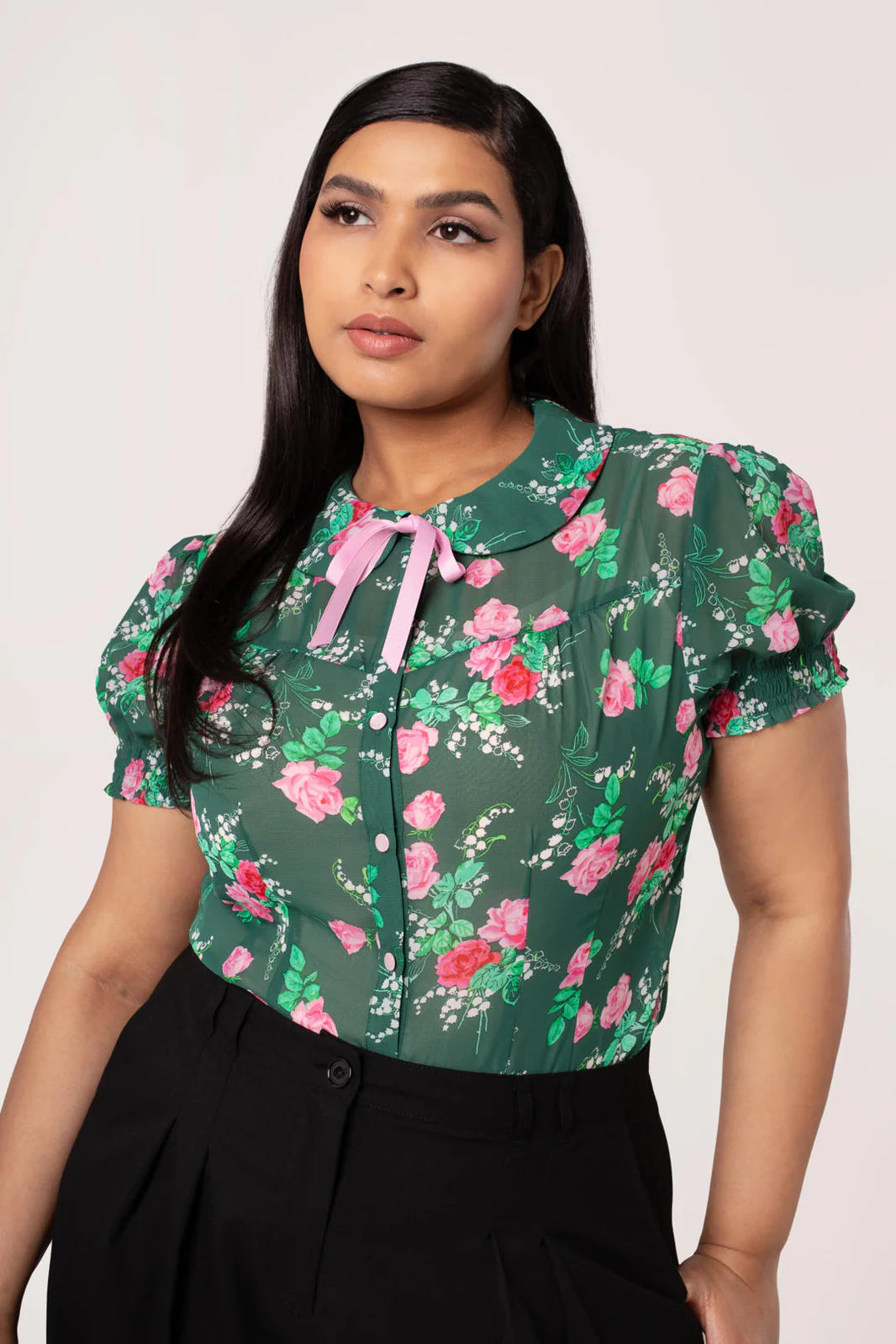 Woman wearing a green floral blouse with pink accents on a plain background