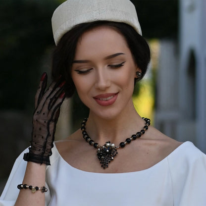 Woman wearing a white dress, black gloves, and a decorative necklace with a blurred background
