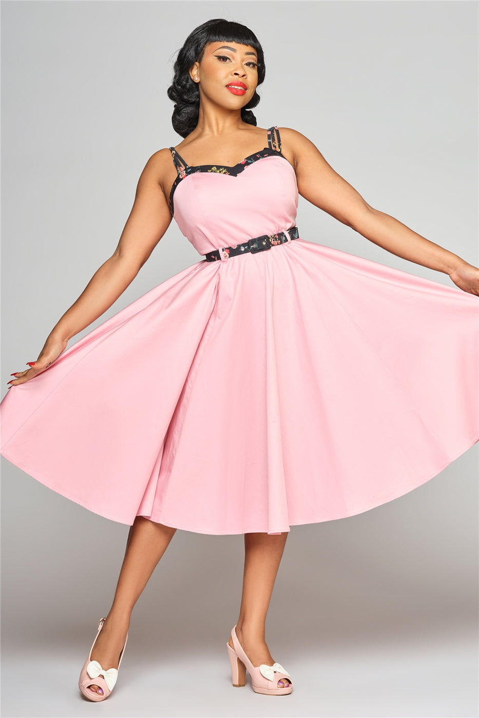 Beautiful dark haired woman standing holding out the skirt of her 50s style pink dress.