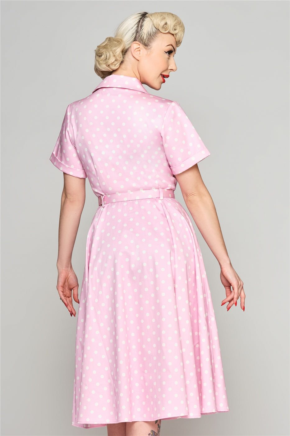 Pretty blonde woman wearing an elegant short sleeved pink and white polka dot shirt dress with a matching belt.