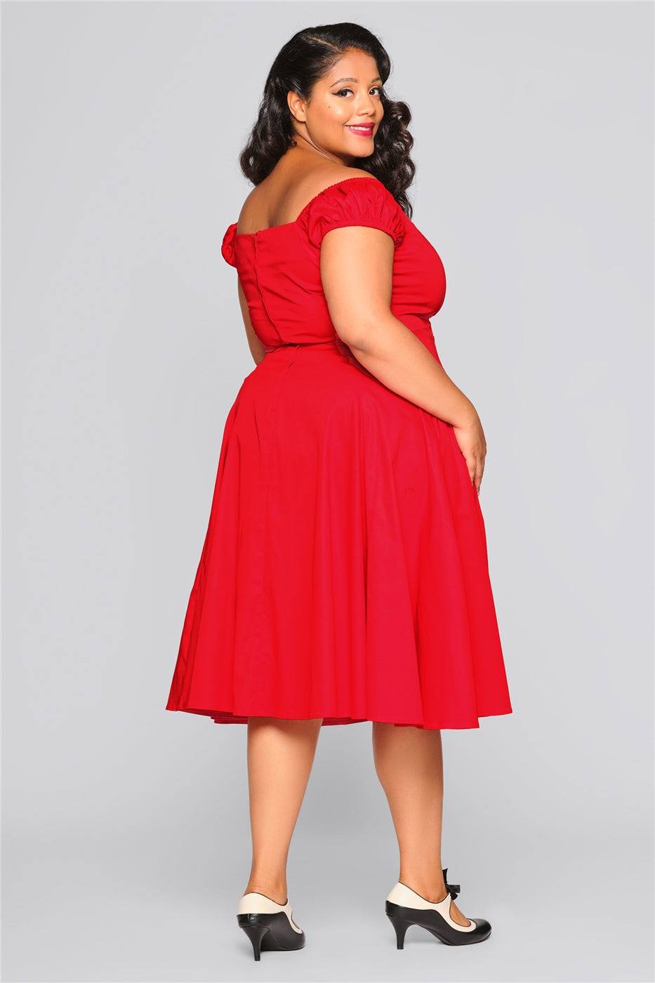 Brunette model smiling, looking over her shoulder wearing a red mid length dress and high heels