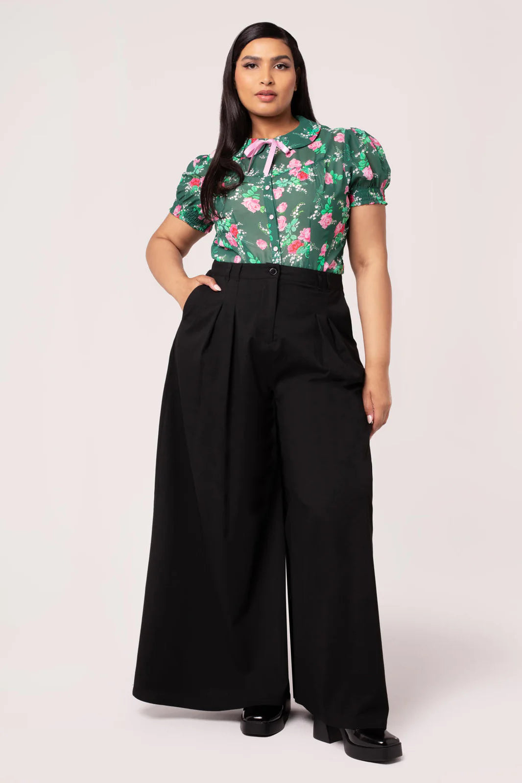 Woman wearing a floral top and black wide-leg pants on a white background