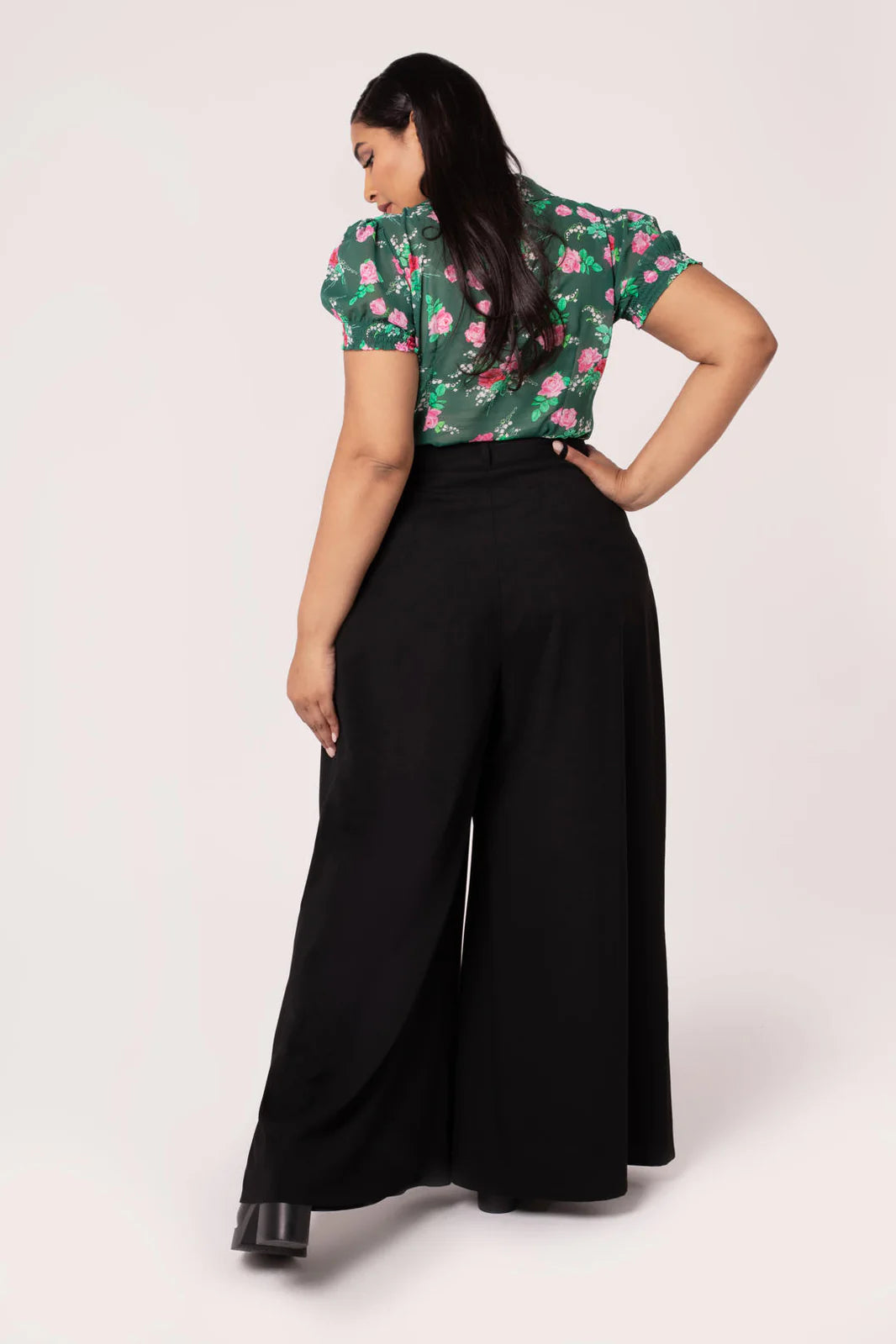 Woman wearing a floral top and black wide-leg pants on a white background