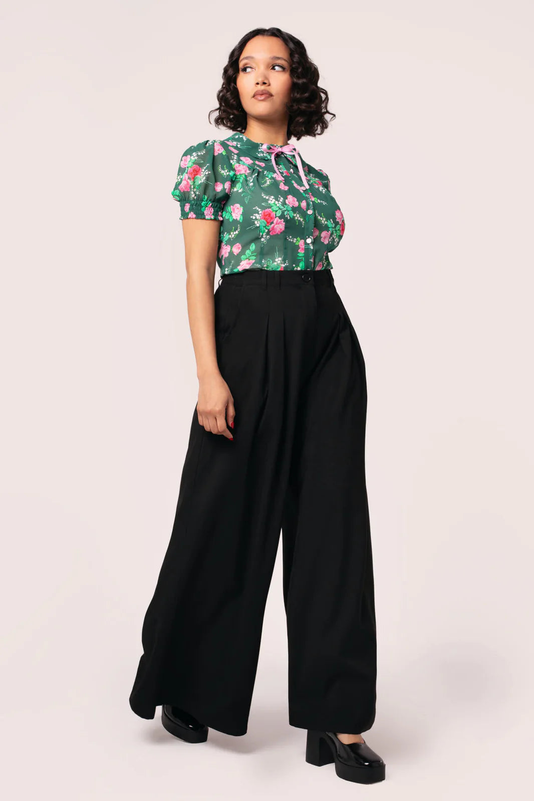 Woman wearing a floral top and black wide-leg pants on a white background