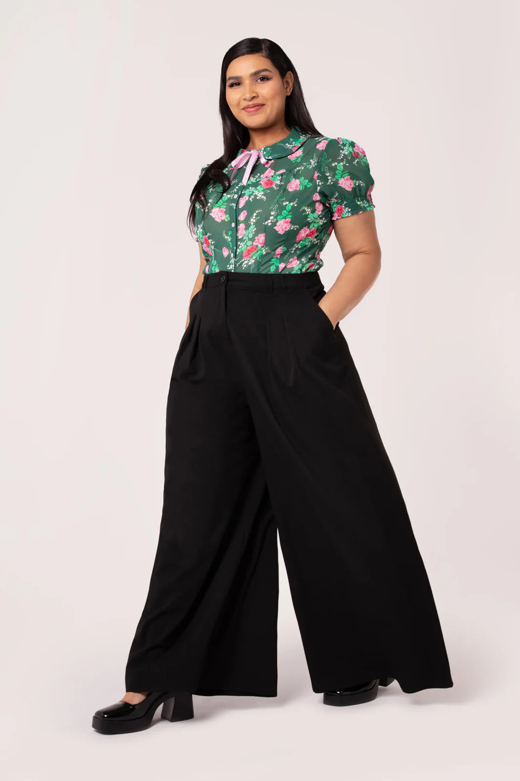 Woman wearing a floral top and black wide-leg pants on a white background