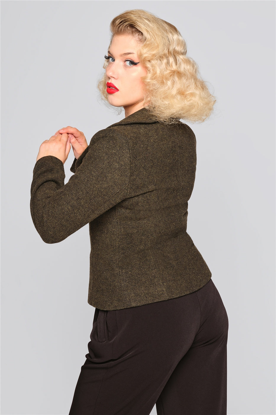 Blonde woman with red lipstick looking over her shoulder wearing the green Molly Riding Jacket by Collectif and black swing trousers