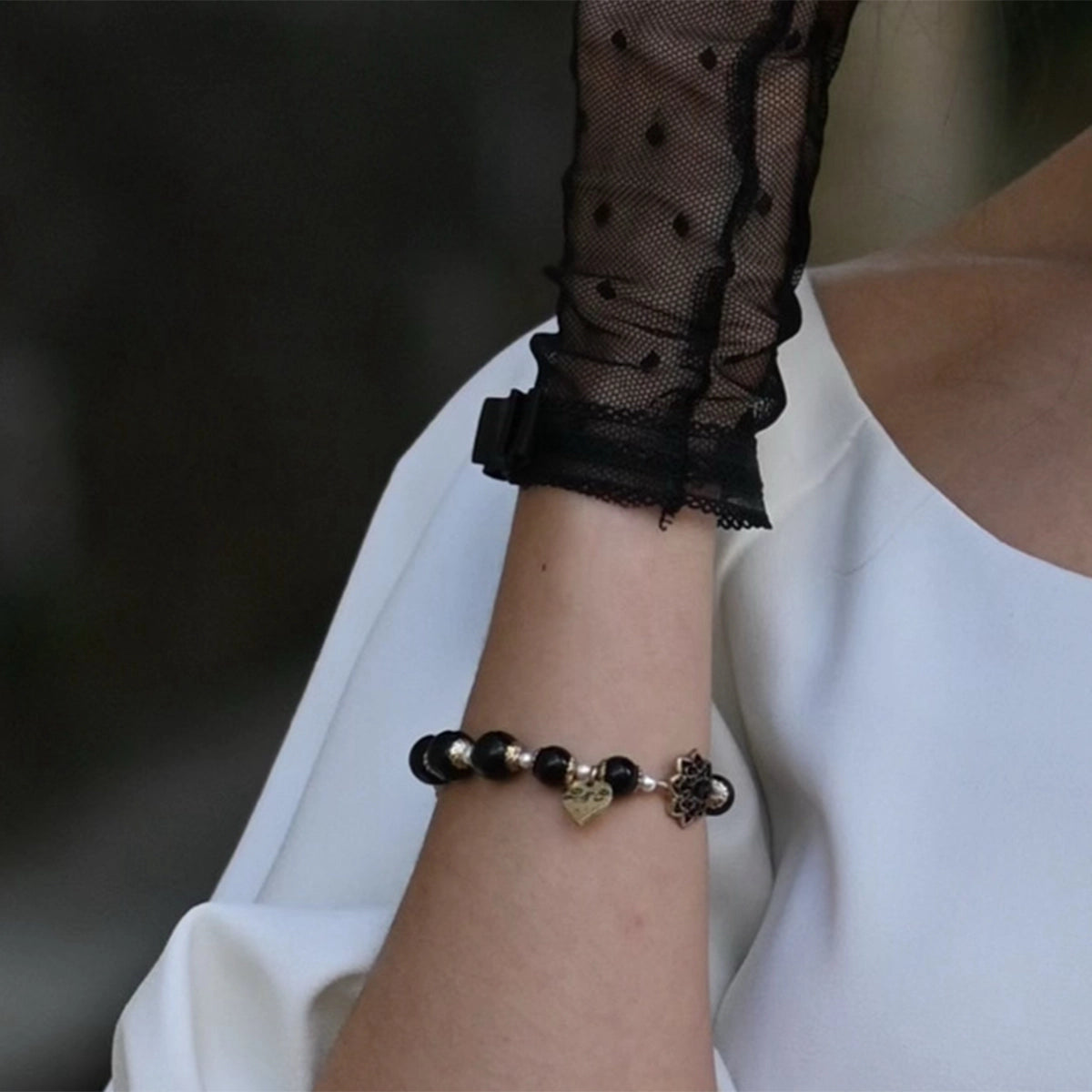 Close-up of a wrist wearing a bracelet with black and gold beads, against a blurred background.