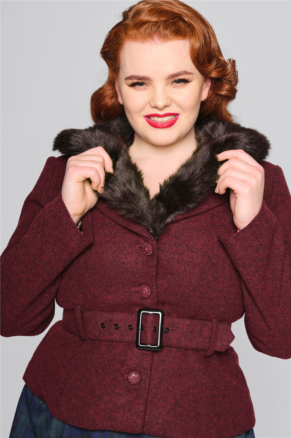 Smiling redhead model holding the fur trim collar on her burgundy jacket