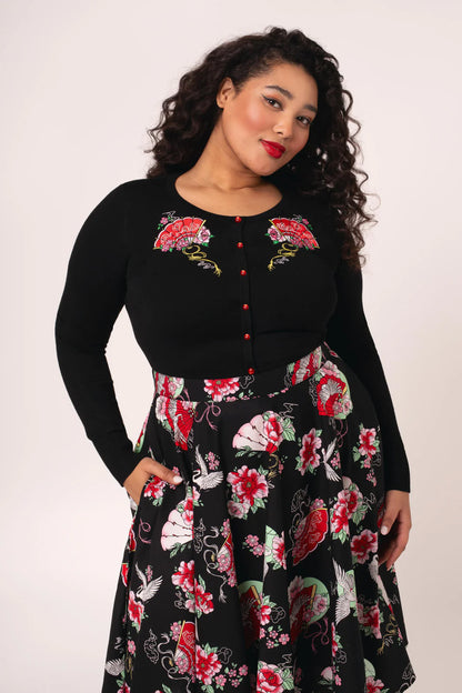 Woman wearing a black cardigan with floral embroidery and a matching floral skirt on a white background