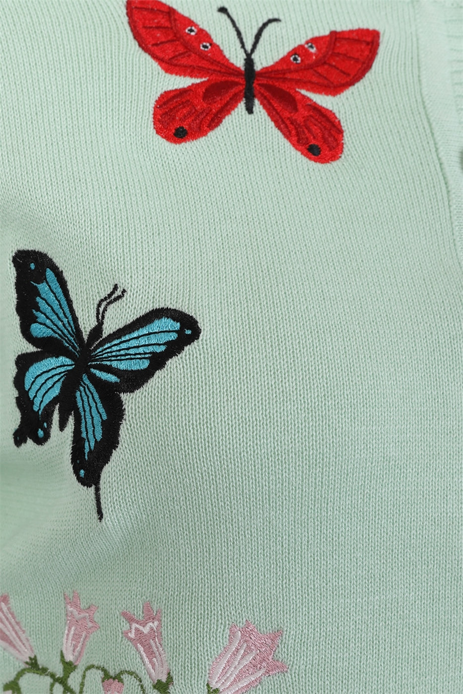 Close up of a blue and black embroidered butterfly and a red embroidered butterfly flying above some pink embroidered flowers with green stems.
