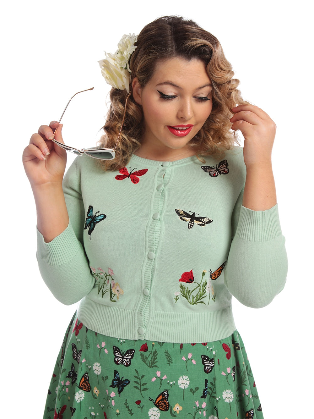 vintage model holding sunglasses wearing a hair flower and mint green cardigan with embroidered colourful butterflies and flowers on the front