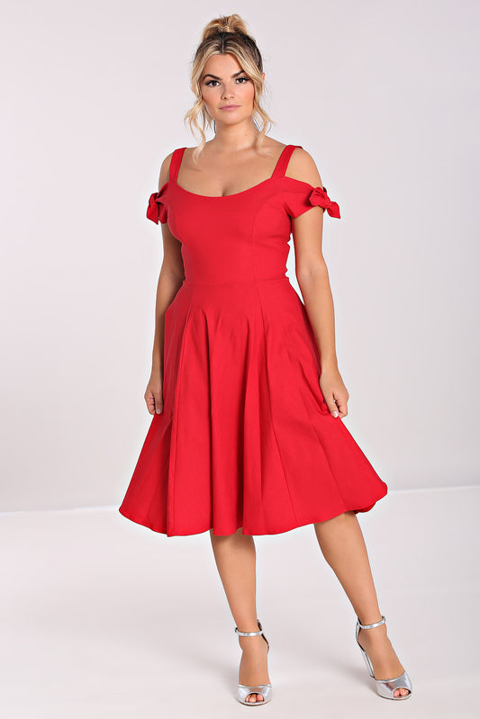 Blonde woman standing with her arms by her sides wearing a strappy red mid length dress with off the shoulder detail and strappy silver heels