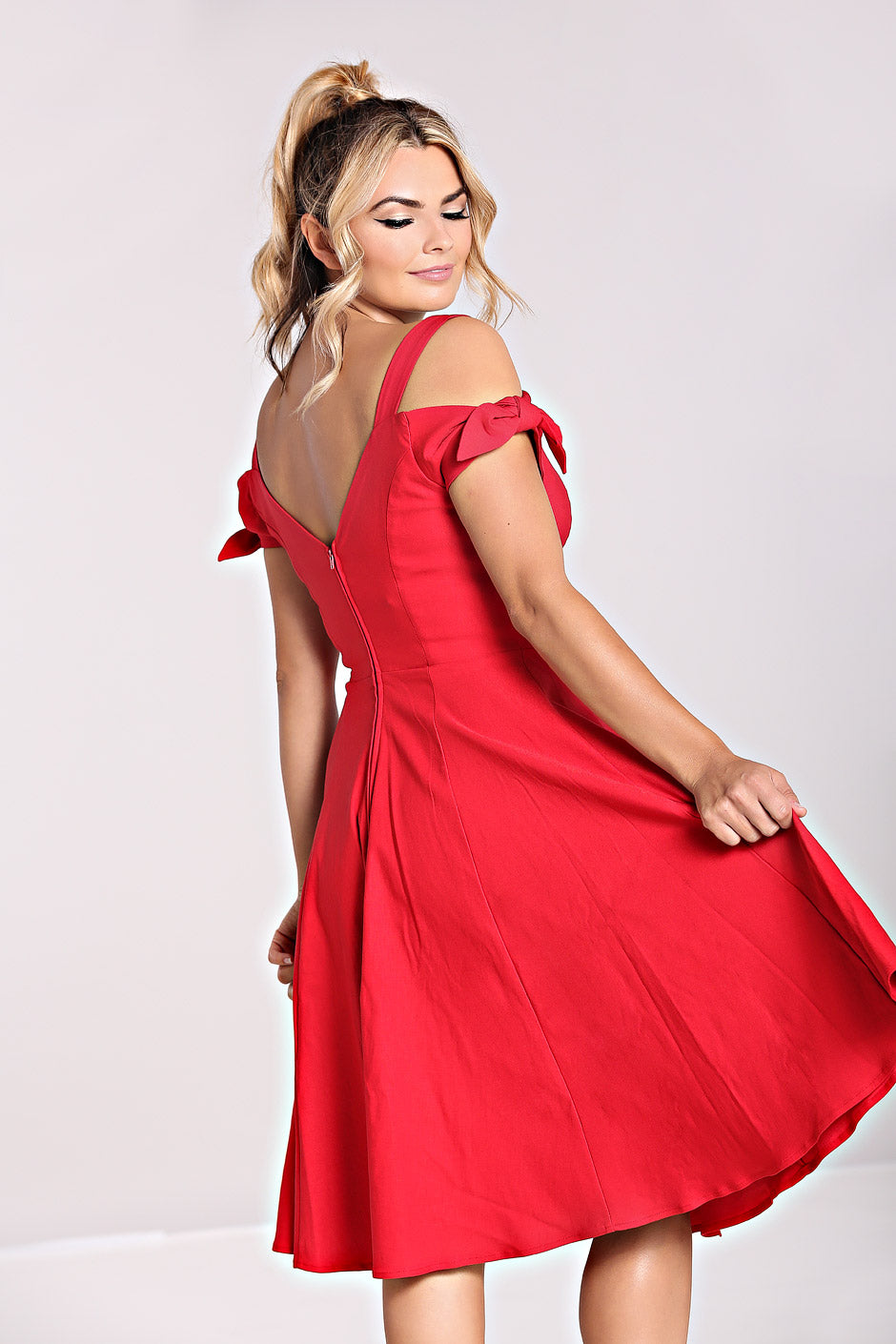 Blonde woman wearing her hair in a ponytail and a red mid length dress, swishing her skirt