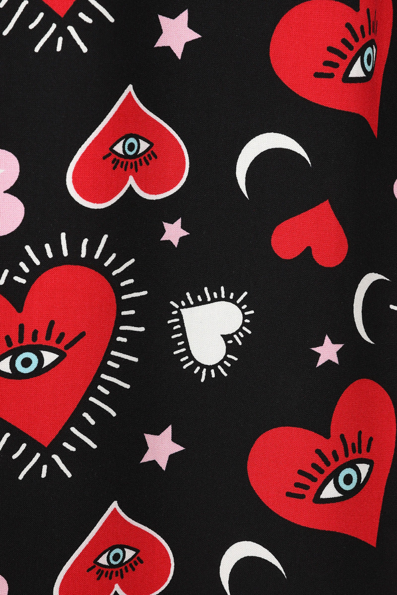 Close up look at the print of the Kate dress. The larger red hearts have eyes in the centre and the background pattern is stars, moons and smaller pink and red heart against plain black.