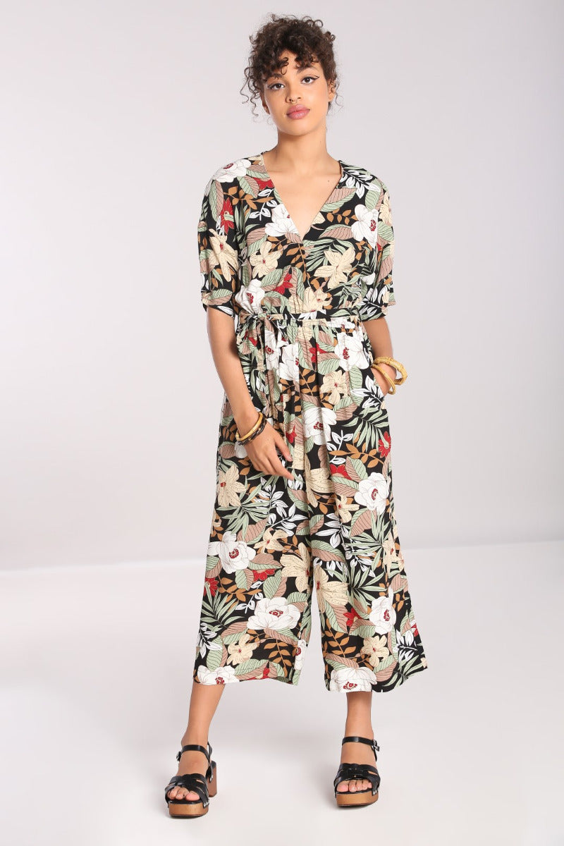 brunette girl with curly hair in an up-do wearing a wide leg floral print V Neck jumpsuit and sandals