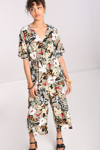 Girl with brown eyes and curly brown hair wearing a summery floral print jumpsuit, wooden carved bangles and sandals