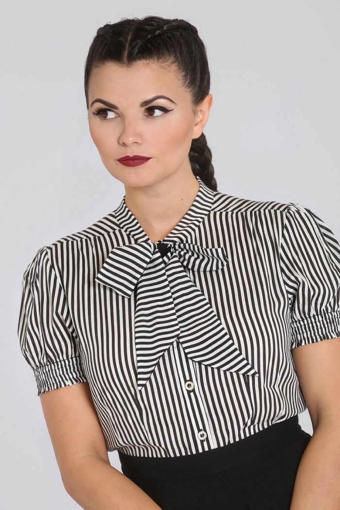 Brunette woman with her hair in a plait looking off to the side wearing the black and white striped pussybow blouse by Hell Bunny and a high waisted black skirt.