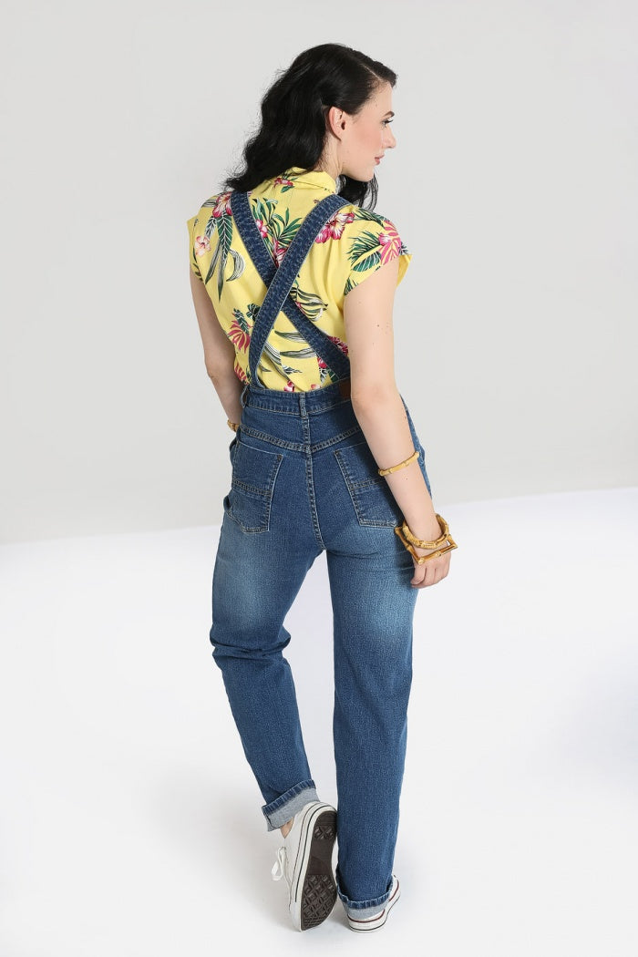 Back view of a dark haired girl weaing a short sleeved floral shirt and denim dungarees