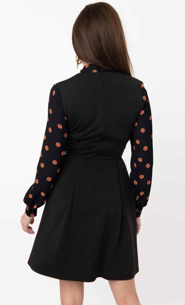 Back view of a brown haired girl wearing a fit and flare black dress with long pumpkin print sleeves
