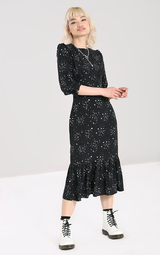 Smiling blonde woman wearing a black mid length dress with zodiac star constellations all over and chunky white boots