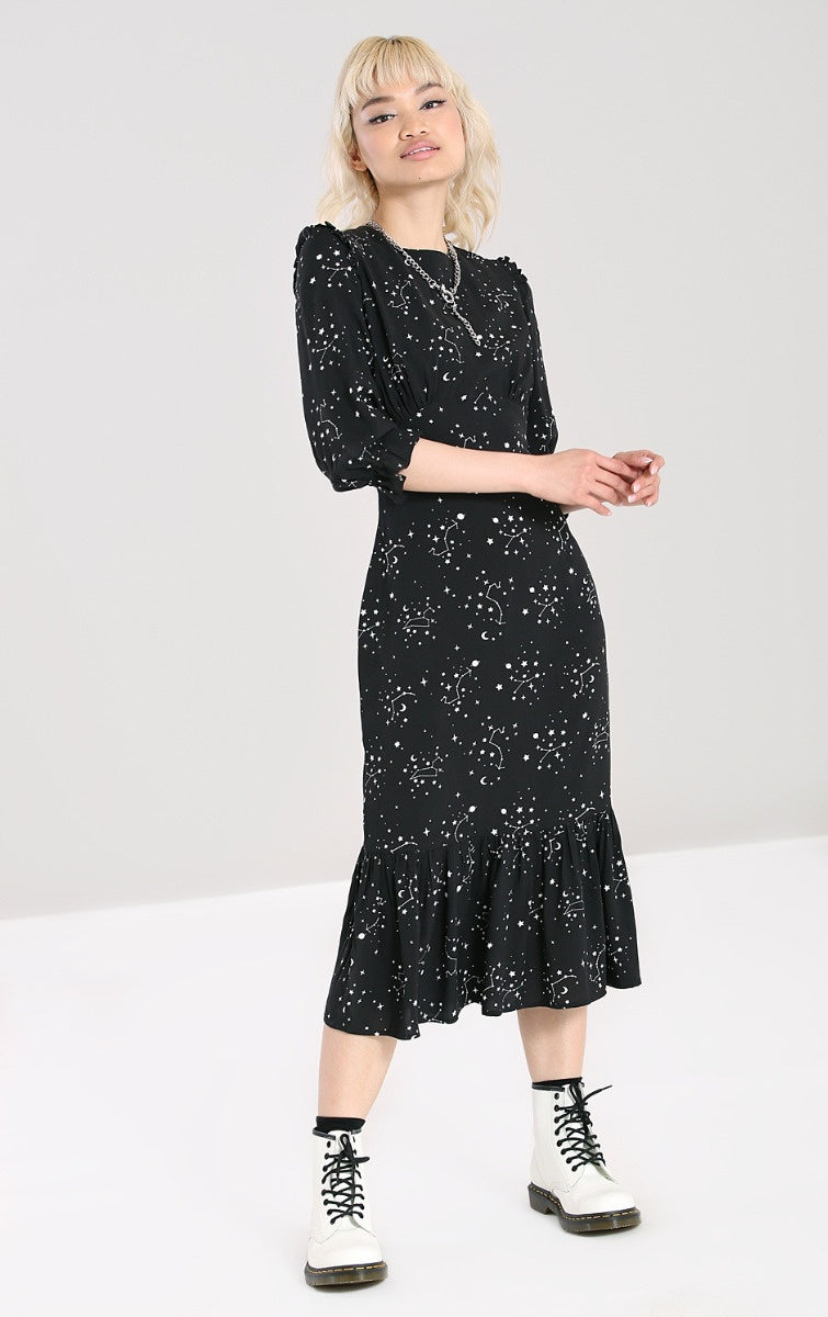 Smiling blonde woman wearing a black mid length dress with zodiac star constellations all over and chunky white boots