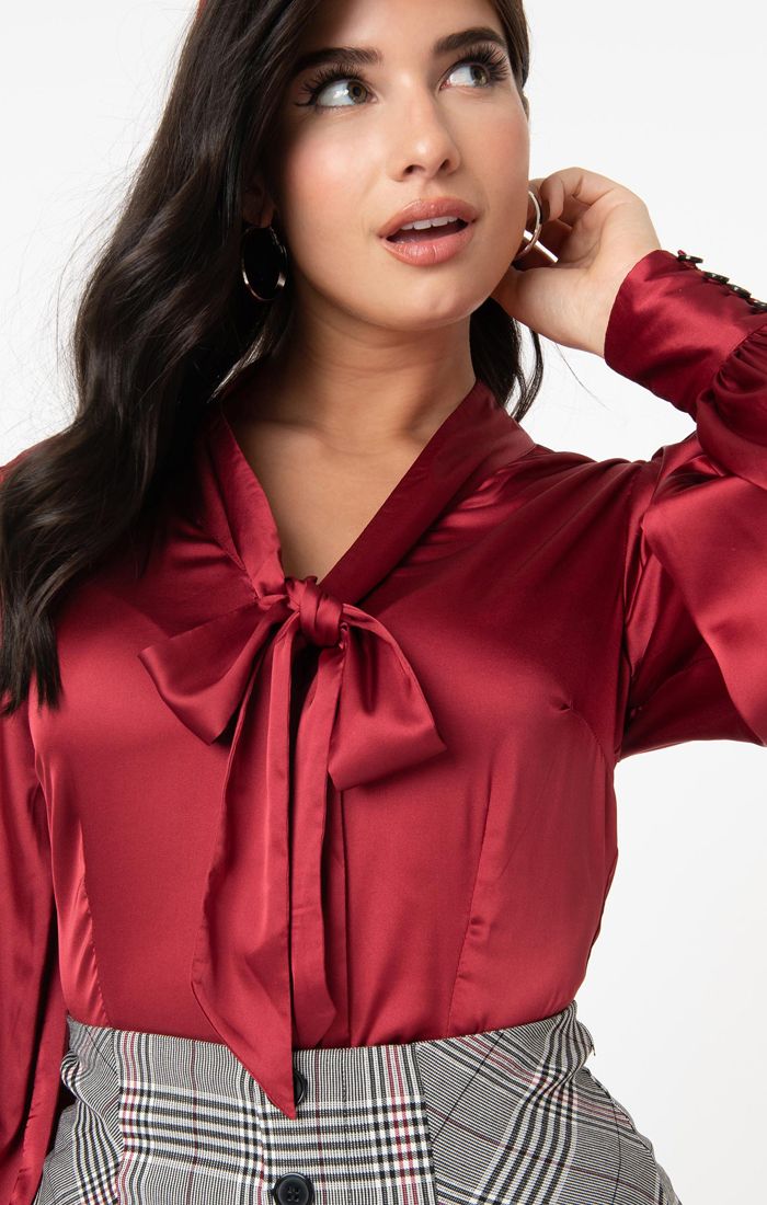 Close up of brunette girl tucking her hair behind her ear wearing a red satin blouse with a pussybow tie neck and high waisted trousers