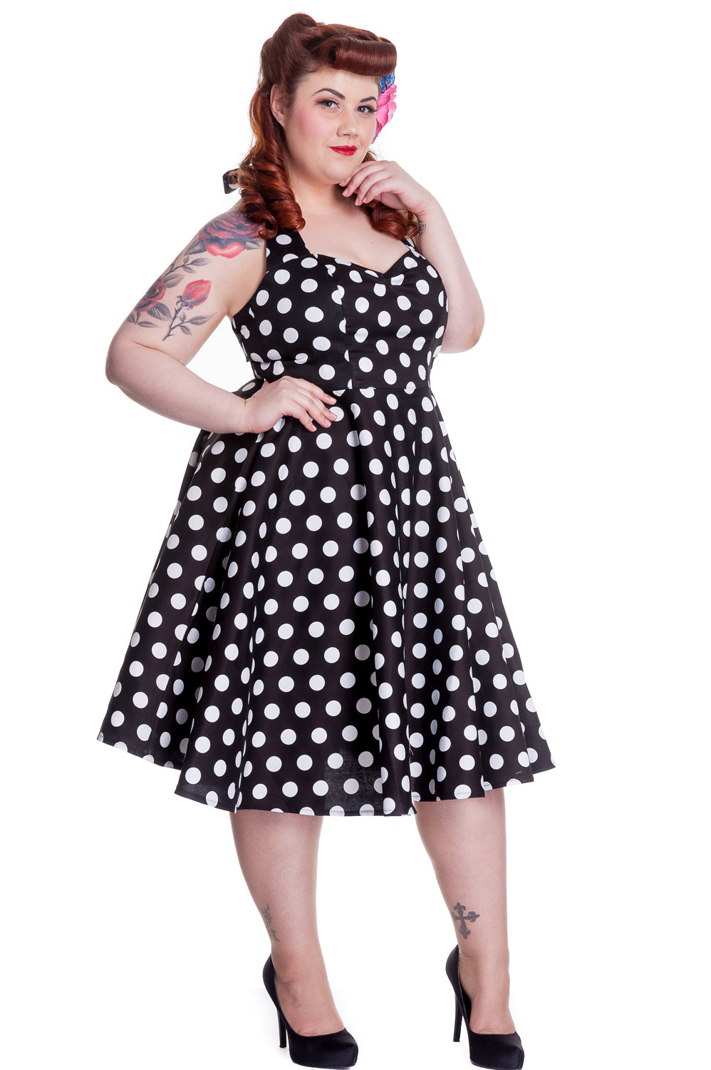 Pinup style model wearing a halter neck polka dress and black stilettos standing with one hand to her face and the other on her hip