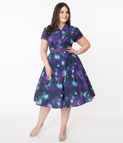 Happy girl with long brown hair wearing a purple galaxy print belted dress with a fitted bodice and flare skirt and sparkly silver high heel shoes standing in front of a white background