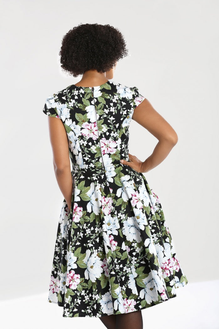 Dark curly haired woman standing with one hand on her hip facing away from the camera  wearing the Alba floral mid dress