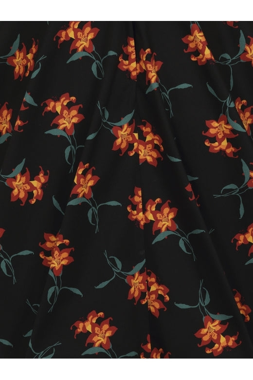 Close up of the skirt of the Trixie Midnight Lily Dress featuring orange lilies with green stems on a black background