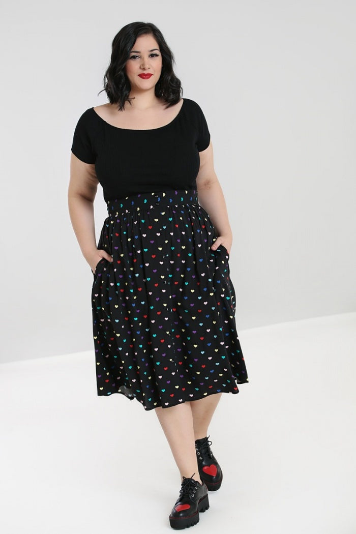 Dark haired model wearing a black top and black skirt with an all over heart print standing with her hands in her pockets