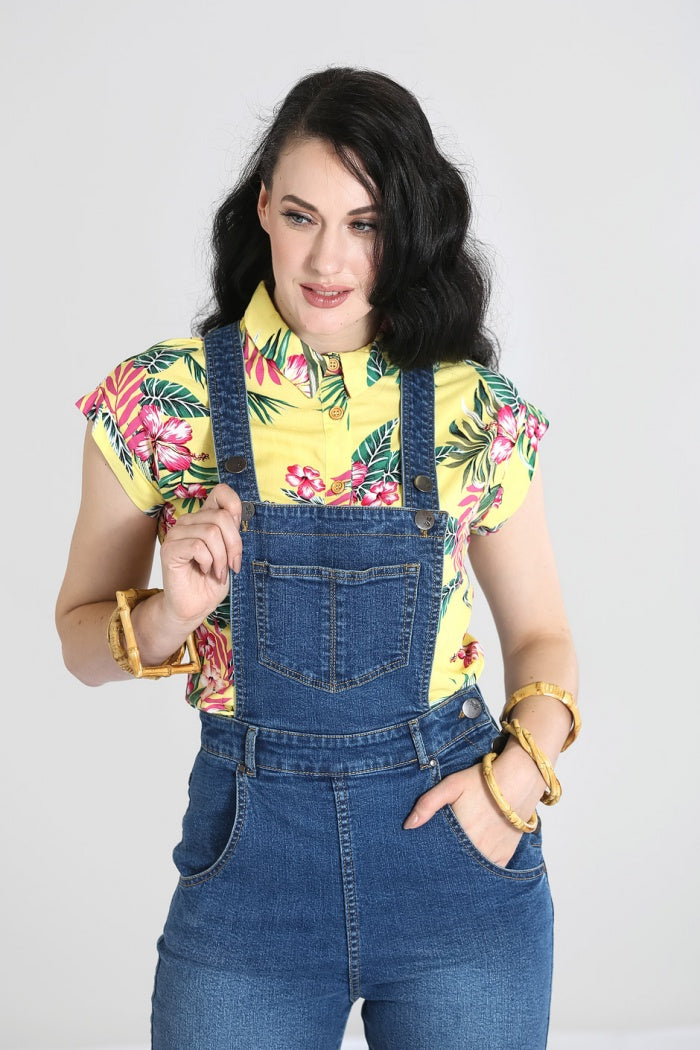 Brunette girl standing with one hand in her pocket and the other hand holding the front pocket of her dungarees