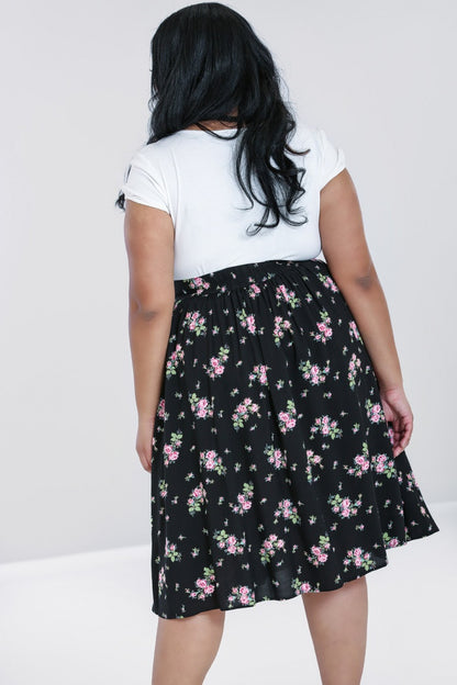 Back view of a brunette model wearing a white top and black skirt with pink floral print