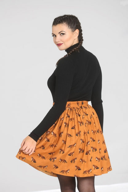 Smiling model wearing her hair in a French braid, a black turtleneck top and a brown/mustard fox print mini skirt which she is holding out to the side